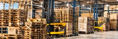Galpão com pilhas de pallets de madeira e empilhadeira amarela